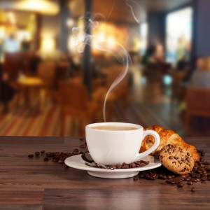Coffee drink served with croissant on wooden table with blur cafeteria as background