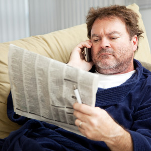 Unemployed man at home on the couch looking at the classified ads in the newspaper.